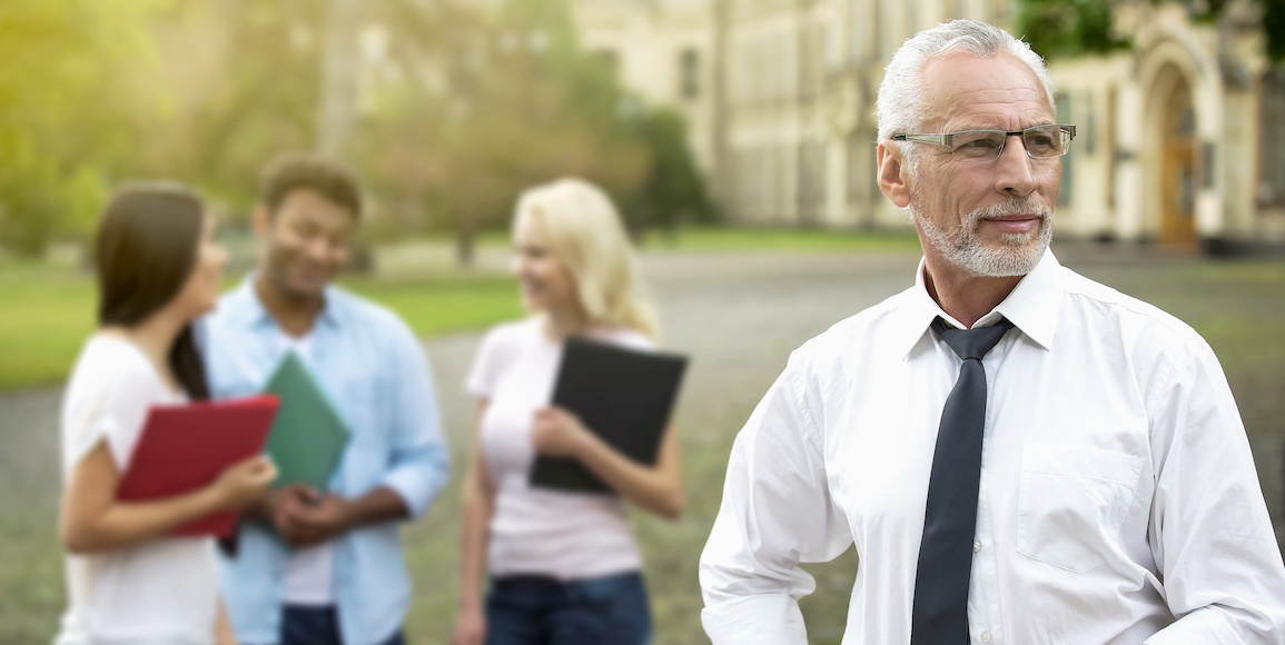 A high school counselor standing in the foreground with three students chatting in the background