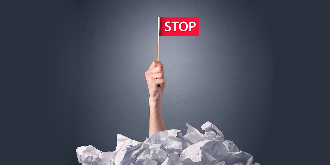 Arm sticking up out of a pile of wadded up paper, holding up a red flag that says “stop”