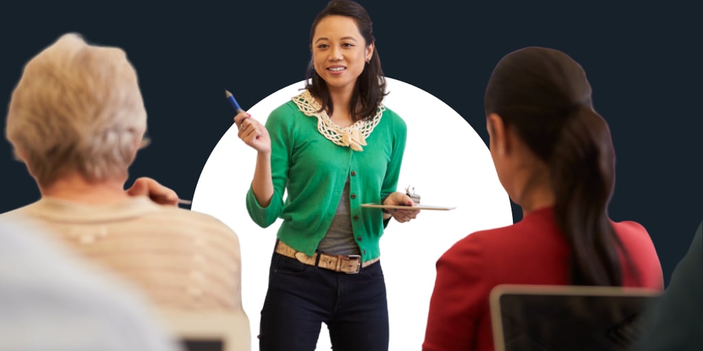 A teacher in bright clothing as she holds a pencil, lecturing to students