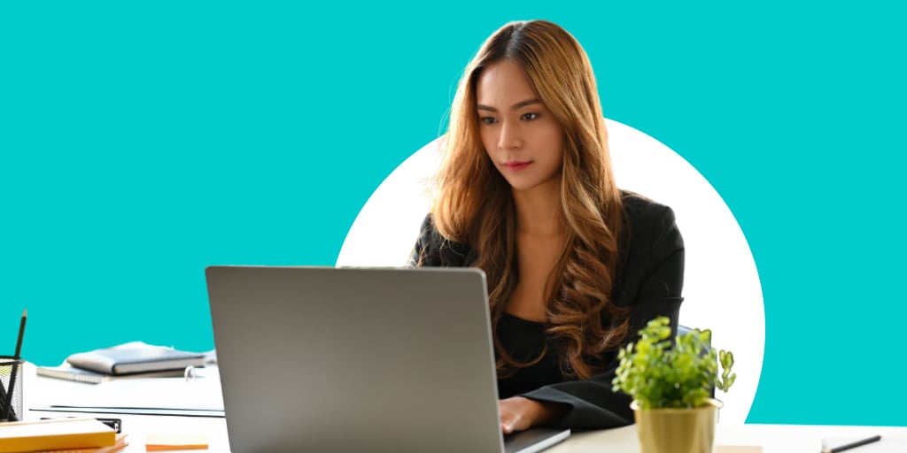 Adult sitting at a desk with a cactus plant, working on their laptop