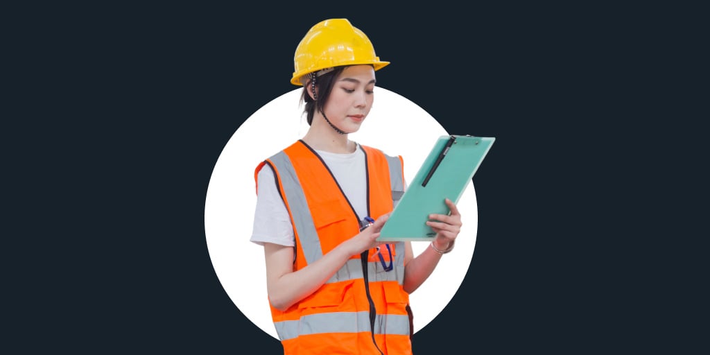 Woman in a hard hat and orange safety vest working and reading