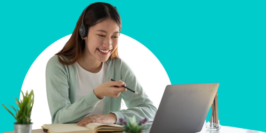 A young woman wearing headphones smiling while working on a laptop