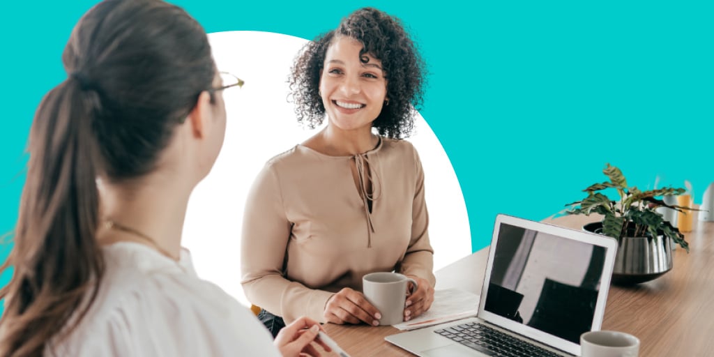 One woman helping another woman as they work in front of a laptop