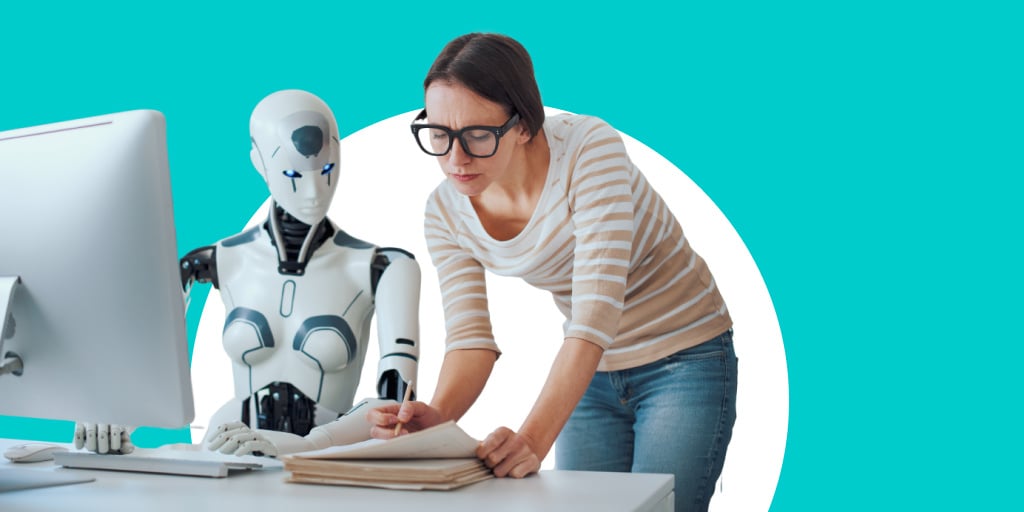 A teacher helping a robot sitting at a desk with work