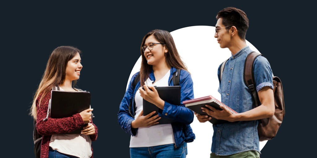 A group of people standing around with books and laptops talking to each other