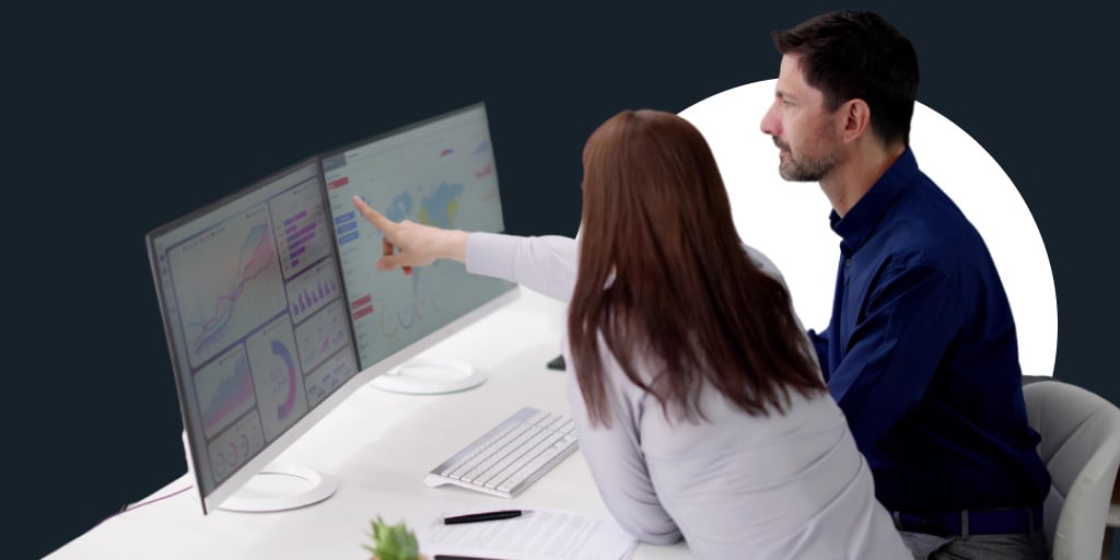 Two workers at a computer sitting next to each other, with one pointing at the screen