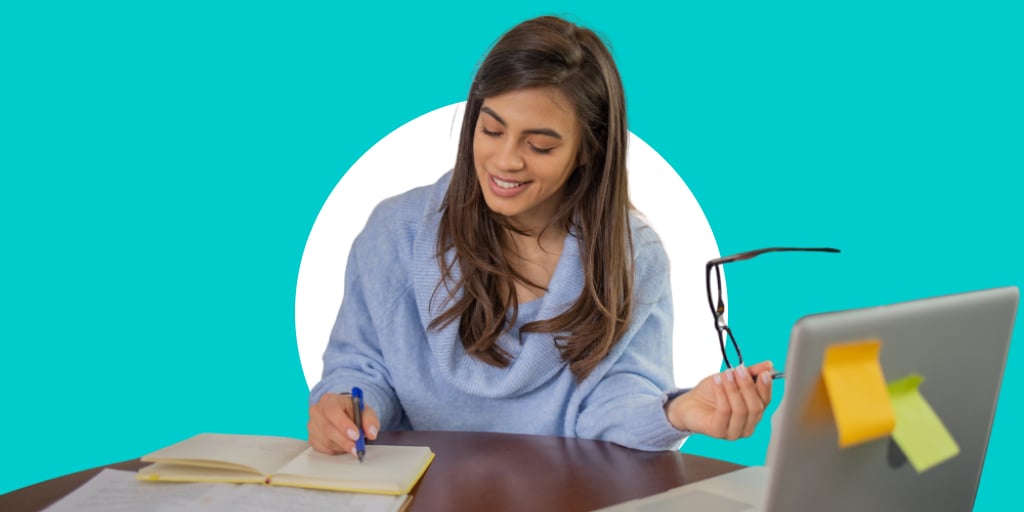 A young worker, with glasses in her hand as she writes onto a notebook