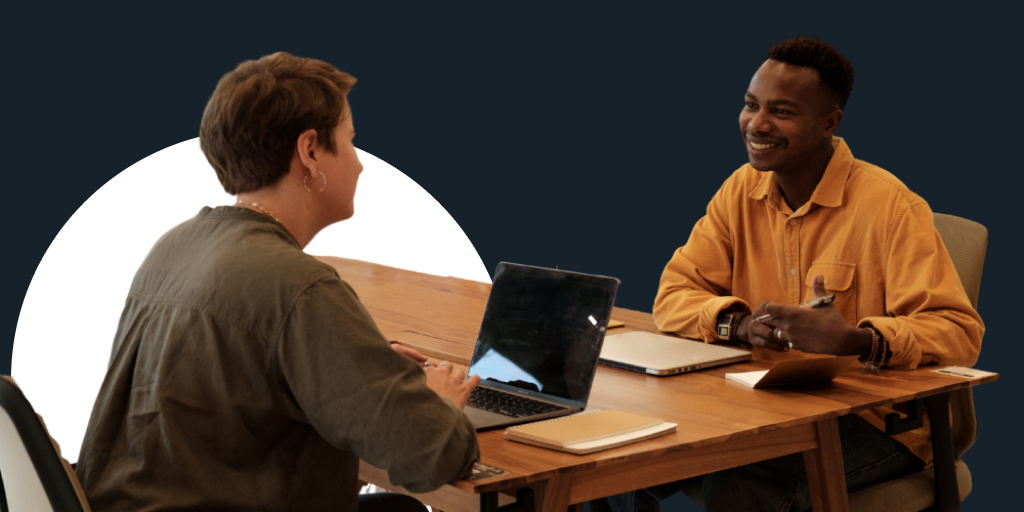 Two people, sitting down across from each other with laptops in front of them