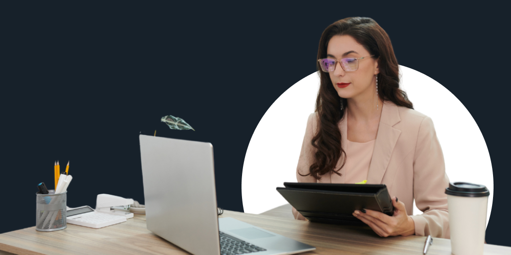 A woman sitting down, filling out notes on a tablet while looking at a laptop
