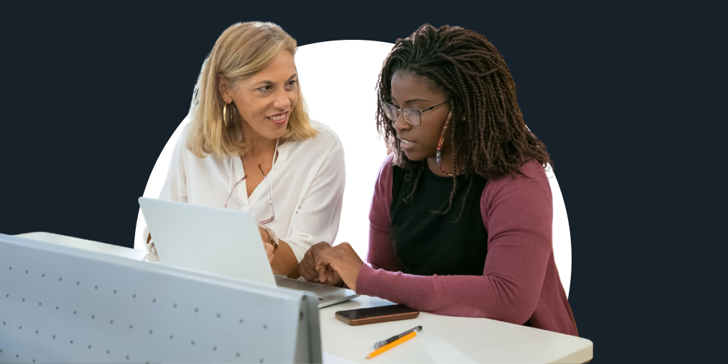 A teacher sitting next to a student, helping them as the work on a laptop