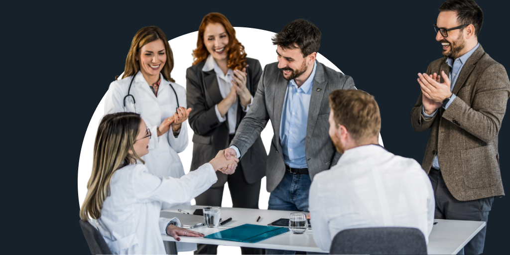 A group of professionals gathered around, as one steps forward, shaking hands with someone across a table