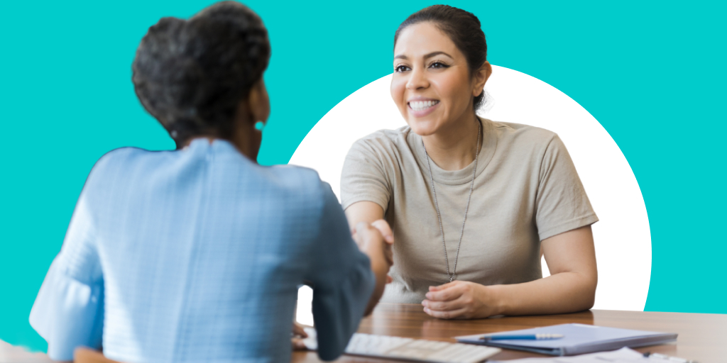 A woman shaking hands with someone across and interview table
