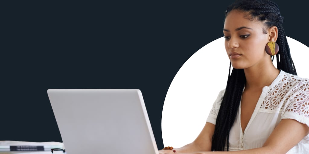 A woman working at a desk, as she types on her laptop
