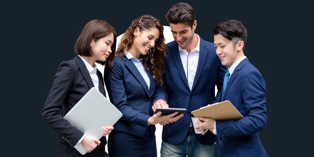 A group of well-dressed individuals all looking at a tablet and notes together while standing