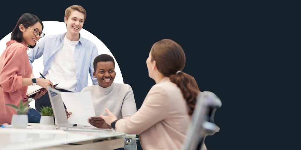 A group of people directed toward a boss or manager sitting in front of them, as they laugh and smile going over some notes