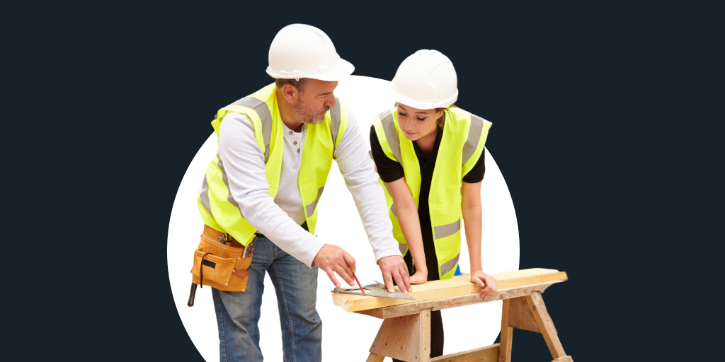 Two workers in construction attire and hats working on a cutting a piece of lumber