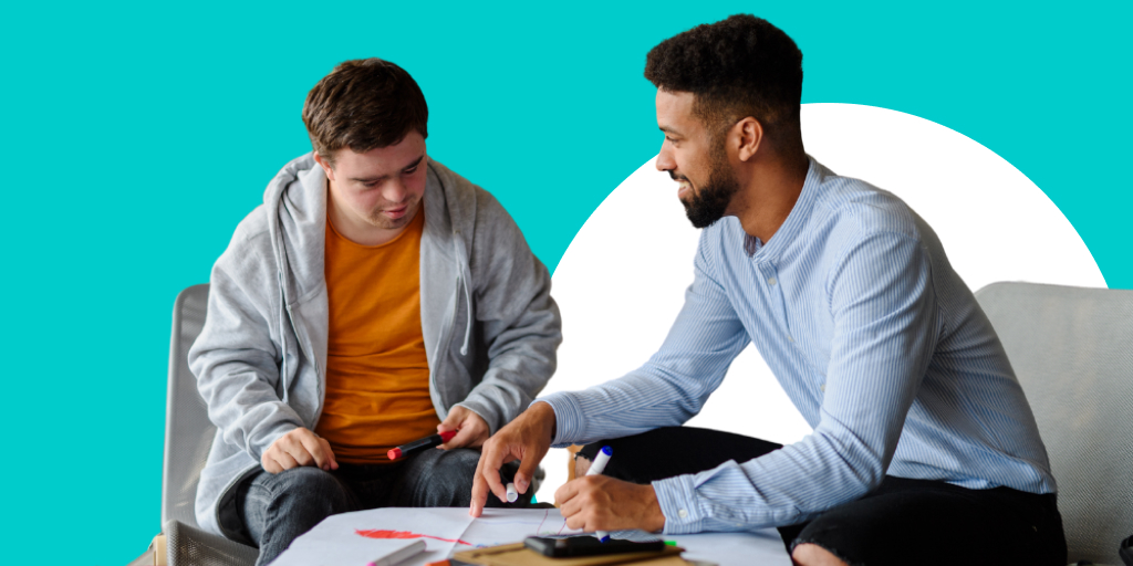 Teacher sitting and working with a student, pointing at a paper on a table in front of them