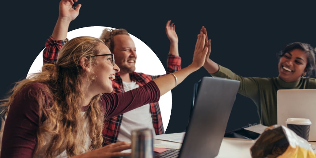 Group of workers sitting and working on computers, all high fiving in the middle.