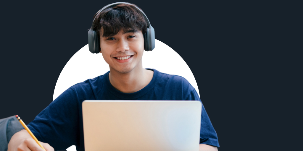 Young adult smiling while sitting and working a laptop with headphones on