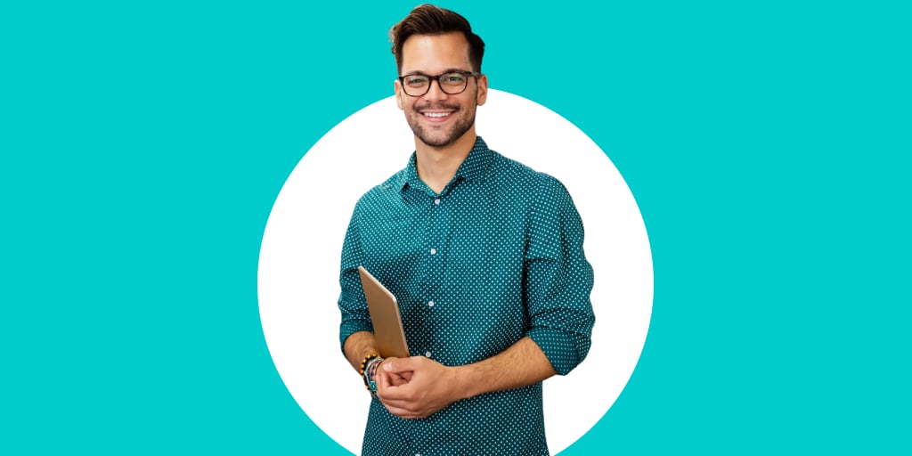 Adult wearing glasses, smiling, as they hold a book