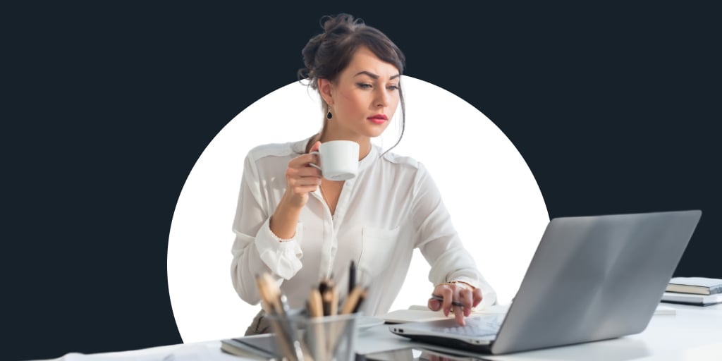 A women dress professionally working on a laptop drinking a coffee