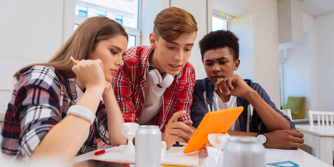 Three students at a desk looking at a tablet together for college and career readiness