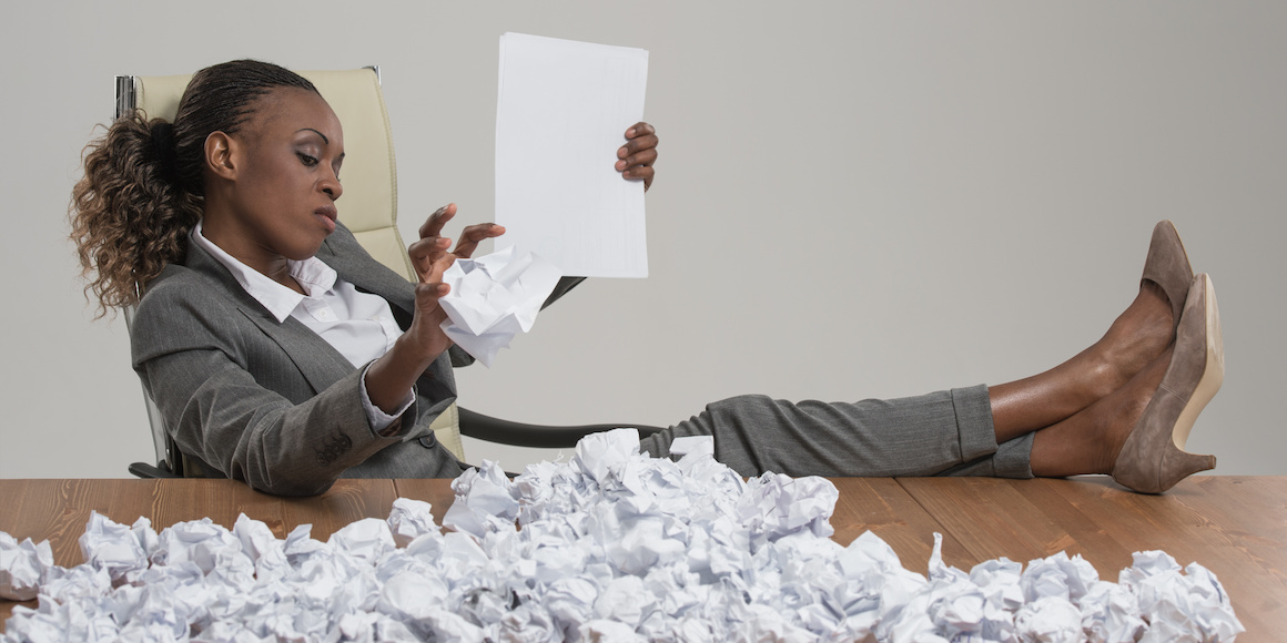 A tired-looking hiring manager with dozens of wadded paper resumes on her desk